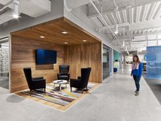 a woman walking through an office lobby with chairs and televisions on the wall in front of her