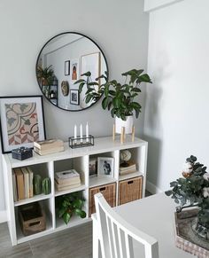 a white table topped with lots of books next to a wall mounted mirror and potted plant