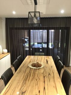 a wooden table topped with a plate of food next to black chairs in front of a window