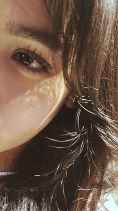 a close up of a woman's face with hair blowing in the wind and sun shining through her eyes