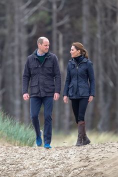 prince william and kate are walking together in the sand, with trees in the background