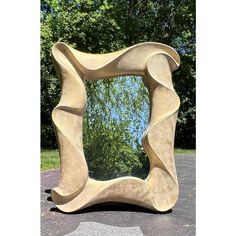 a large mirror sitting on top of a cement slab in front of a tree filled park