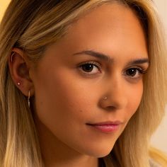 a close up of a person with long blonde hair and wearing earrings, looking at the camera