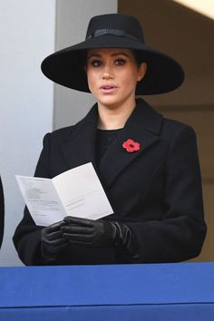 a woman in a black hat and coat holding a piece of paper