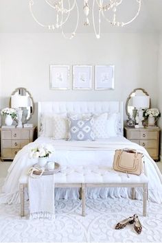 a bedroom with white bedding and chandelier hanging from the ceiling above it