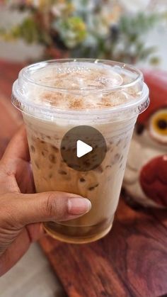 someone holding up a cup of iced coffee with an owl figurine in the background