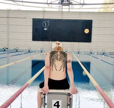 a woman sitting on top of a chair next to a swimming pool with a clock above her back