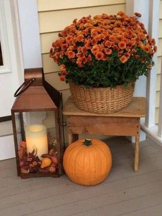 a basket full of flowers sitting next to a lantern and pumpkin on the front porch