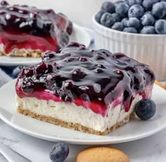 two pieces of cheesecake on plates with blueberries and cookies in the foreground