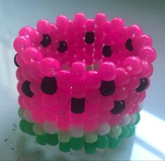 a pink and green bracelet with black dots on the inside is sitting on a white surface