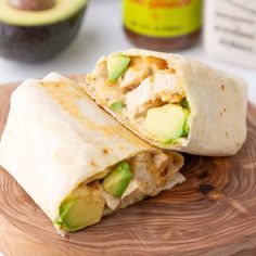 two burritos sitting on top of a wooden cutting board next to an avocado