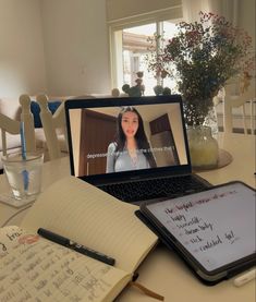 a laptop computer sitting on top of a table next to a note pad and pen