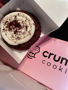 a chocolate cookie with white frosting in a pink box on top of a table