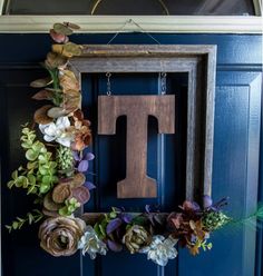 a wooden letter hanging on a blue door decorated with flowers and greenery in front of it