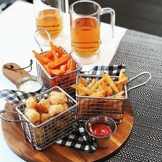 three baskets filled with food sitting on top of a wooden tray next to cups and sauces