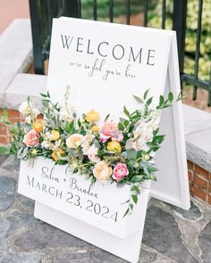 a welcome sign with flowers and greenery on it