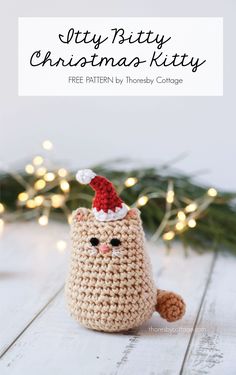 a crocheted christmas kitty sitting on top of a wooden table with lights in the background