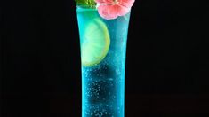 a tall glass filled with blue liquid and pink flowers on top of it, next to a lime slice