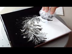 someone is painting on a piece of paper with white paint and silver feathers in it