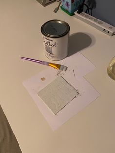 a can of paint sitting on top of a table next to a brush and paper