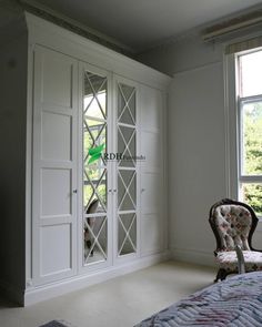 a chair sitting in front of a window next to a white cabinet with glass doors