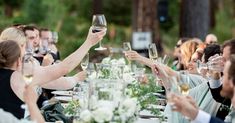 a group of people sitting at a table with wine glasses in their hands and flowers on the table