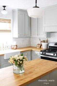 a vase with flowers sitting on top of a wooden counter in a kitchen next to an oven