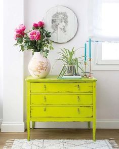 a bright green dresser with flowers on top in a white and pink living room area