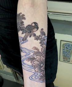 a woman's arm with a bird and flowers tattoo on her left arm, along with water