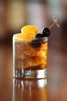 an old fashioned cocktail is garnished with black olives and orange peels