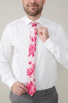 a man wearing a white shirt and tie with pink flowers on it is posing for the camera