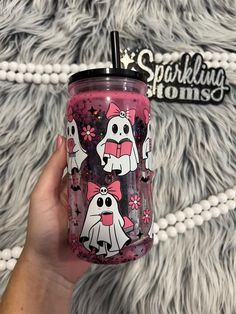 a hand holding a pink tumbler with two ghostes on it