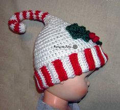 a crocheted white and red hat with green leaves on the top, sitting on a mannequin's head