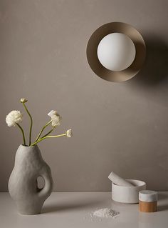 a white vase with flowers in it next to a wall light and some other items