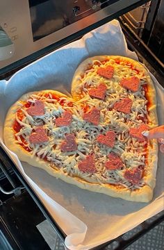 a heart shaped pizza sitting on top of a pan next to an open oven door