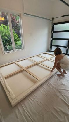 a woman kneeling on top of a bed in a room with white walls and windows