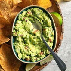 a bowl filled with guacamole surrounded by tortilla chips and lime wedges