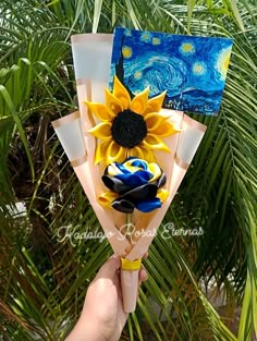 a hand holding up a fake sunflower on top of a palm tree