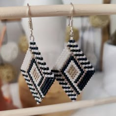 a pair of beaded earrings hanging from a wooden stick on a table next to a vase