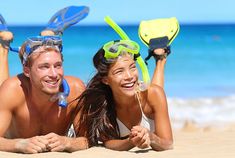 a man and woman laying on the beach with snorkels attached to their heads