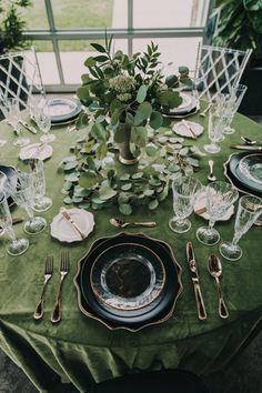 a table set with plates, silverware and greenery in front of a window