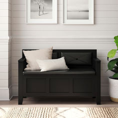 two framed pictures hang on the wall above a black bench with white pillows and throw pillows