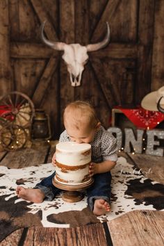 a baby sitting on the floor with a cake in front of him and an animal head