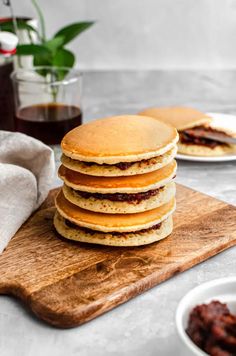 a stack of pancakes sitting on top of a wooden cutting board next to some sauce