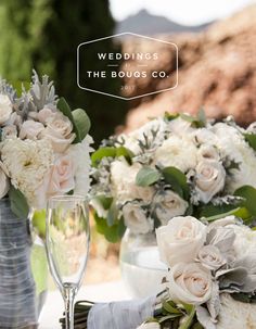 the table is set with white flowers and silver vases for wedding guests to drink