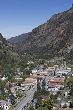 an aerial view of a town with mountains in the back ground and trees on either side