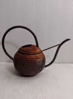 an old teapot is sitting on a white surface with a long handle and curved top