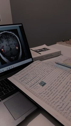 an open laptop computer sitting on top of a desk next to notebooks and papers