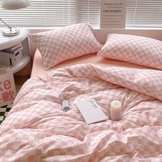 a pink and white checkered comforter on top of a bed next to a window