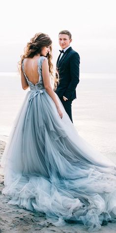 a man standing next to a woman in a blue dress on top of a beach